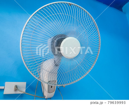White electric fan is mounted on a blue cement wall.  79639993