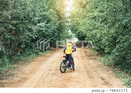 Boy in vest rides on modern bicycle on rural road Boy in vest rides on modern bicycle on rural road 79641575