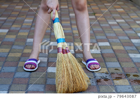 Little girl sweeping cobblestone floor using straw broom. 79643087
