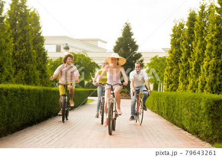 Happy friends riding bicycles on road in park. Happy friends riding bicycles on road in park. 79643261