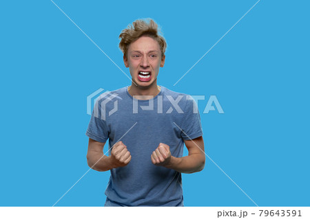 Crazy irritated teen boy is shouting on blue background. 79643591