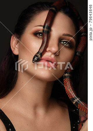 Beautiful girl brunette model with evening fashion make-up with a snake in her hands. Beauty face. Beautiful girl brunette model with evening fashion make-up with a snake in her hands. Beauty face. 79643646