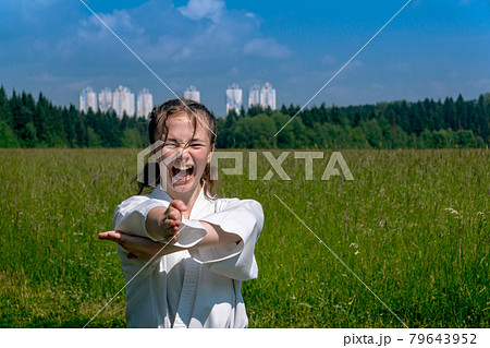 teenage girl training karate kata outdoors, performs nukite tsuki strike with kiai scream 79643952