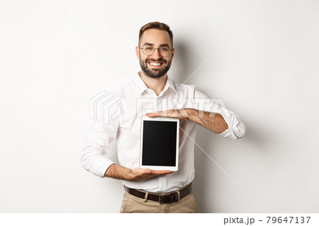 Smiling manager showing something on digital tablet screen, demonstrating website, standing over white background Smiling manager showing something on digital tablet screen, demonstrating website, standing over white background 79647137