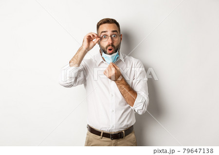 Covid-19, social distancing and quarantine concept. Impressed business man take off medical mask, looking surprised, standing over white background 79647138