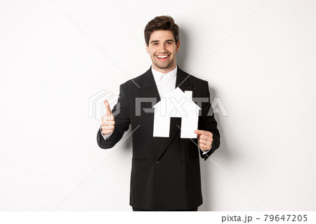 Portrait of confident real estate agent showing house maket and thumb-up, standing against white background Portrait of confident real estate agent showing house maket and thumb-up, standing against white background 79647205