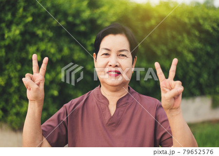 Mature asian woman standing and showing 2 fingers at public park,Happy and smiling,Senior care insurance concept 79652576