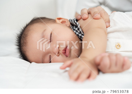 baby sleeping on bed with hand patting 79653078