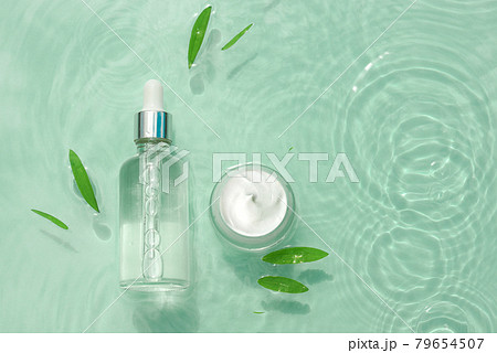 Set moisturizing cosmetics on water with drops. Glass bottle with serum, jar cream on aqua surface 79654507