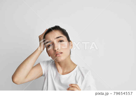 brunette in a white t-shirt holding her head discontent depression pain 79654557
