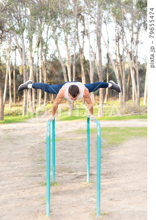 Male athlete exercising on parallel bars in forest. 79655474