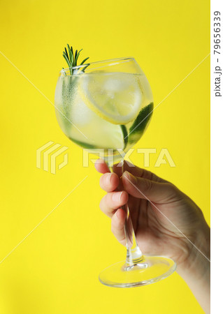 Female hand hold glass of cocktail with citrus and rosemary on yellow background 79656339