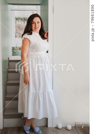 attractive woman in white dress stands in the doorway by the stairs.  79661890