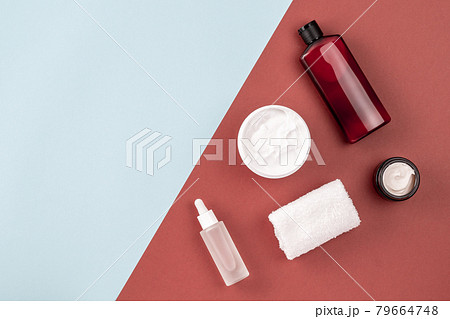 Skin care products on brown and blue surface. Frame from shampoo or cosmetic lotion bottle, towel, open cream jar, serum with peptides. Beauty, spa composition. Flat lay, layout, copy space 79664748