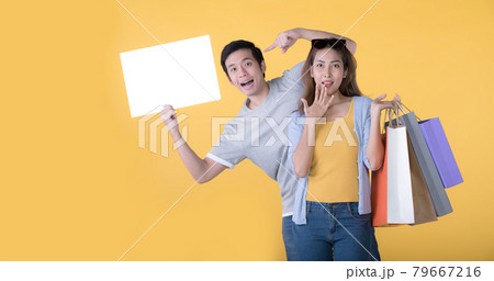 Asian couple holding blank billboard and shopping bags isolated on yellow background 79667216