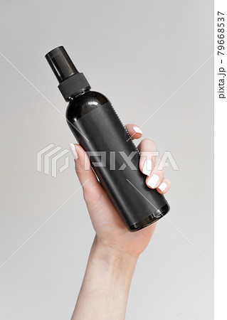 A black bottle of cosmetics in a woman's hand on a light background A black bottle of cosmetics in a woman's hand on a light background 79668537