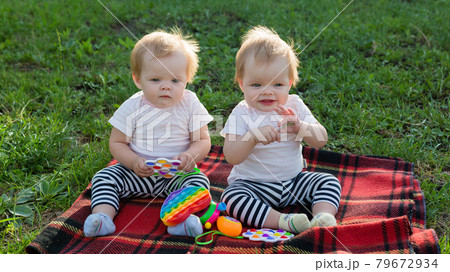 Twin girls play with bright toys on a blanket in a city park Twin girls play with bright toys on a blanket in a city park 79672934