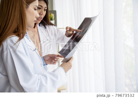 Two asian women doctors discuss meeting doctor's office medical clinic looking x-ray film consulting patient disease. Asian medical lab young women talking together discussing healthcare teamwork 79673532