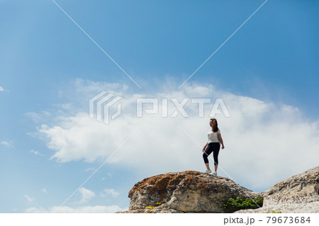 brunette woman standing on a cliff looking at the nature of the journey 79673684