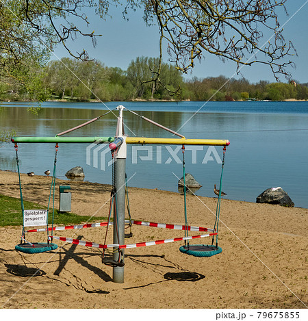 Closed children's carousel on the shore of a leisure lake, sign with German inscription: playground closed 79675855