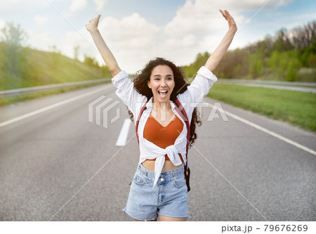 Excited young woman walking along highway, lifting hands up and shouting, feeling happy and free on summer journey 79676269