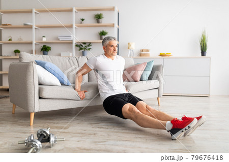 At home workout routine. Sporty mature man leaning on sofa and doing push-up exercises, working out in living room At home workout routine. Sporty mature man leaning on sofa and doing push-up exercises, working out in living room 79676418