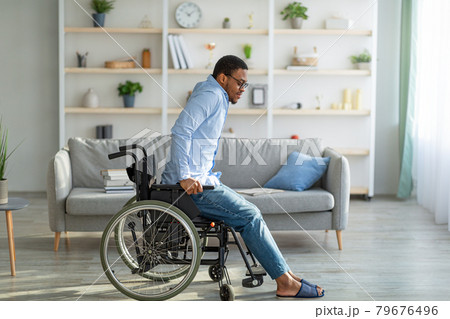 Disabled young black guy trying to get up from wheelchair at home, copy space Disabled young black guy trying to get up from wheelchair at home, copy space 79676496