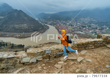 Young girl tourist rejoices posing against the backdrop of an amazing natural landscape. The confluence of two rivers in the city of Mtskheta in Georgia Young girl tourist rejoices posing against the backdrop of an amazing natural landscape. The confluence of two rivers in the city of Mtskheta in Georgia 79677338