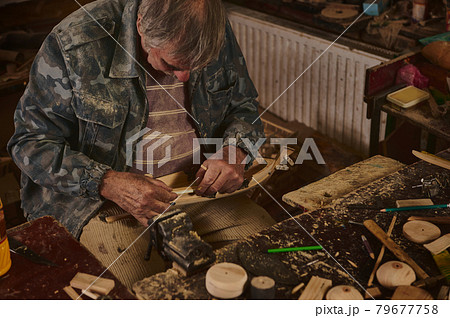 Master-class on making wooden toys. Hands of a wood carving master with a chisel and a wooden workpiece. 79677758