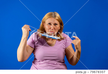 Middle blonde woman taking off her medical mask isolated on blue background Middle blonde woman taking off her medical mask isolated on blue background 79678307
