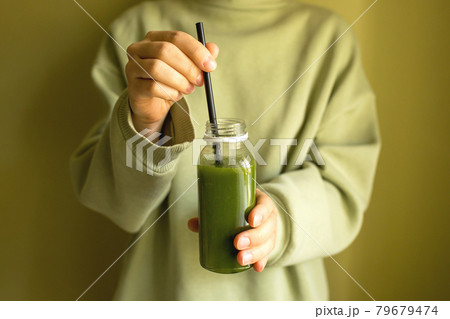 A woman is holding a bottle of green freshly squeezed vegetable or fruit juice. 79679474
