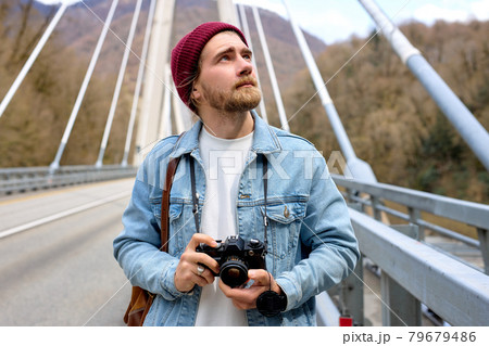 Hipster male in denim jacketwalking on bridge in countryside using camera Hipster male in denim jacketwalking on bridge in countryside using camera 79679486