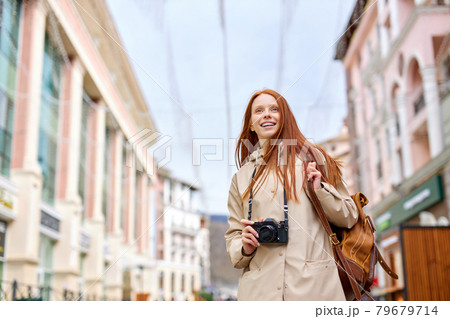 Young smiling woman tourist walks around city in spring, holds retro camera Young smiling woman tourist walks around city in spring, holds retro camera 79679714