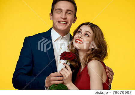 A romantic man hugs a woman in a red dress with a rose in his hand on a yellow background A romantic man hugs a woman in a red dress with a rose in his hand on a yellow background 79679907
