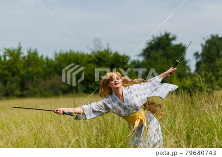 Young asian woman in traditional kimono trains fighting techniques with katana sword Young asian woman in traditional kimono trains fighting techniques with katana sword 79680743