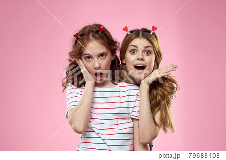 Happy sisters are having fun on a pink background and heart-shaped clothespins on their heads 79683403