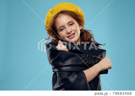 Fashionable girl in a yellow beret and leather jacket striped T-shirt blue background 79683408