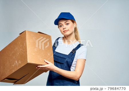 A woman in a working uniform with a box in the hands of a delivery service delivery service light background A woman in a working uniform with a box in the hands of a delivery service delivery service light background 79684770