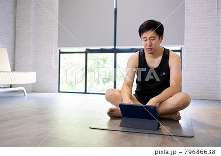 Young man exercising at home while watching a video tutorial on tablet. Male fitness guy training indoors online Young man exercising at home while watching a video tutorial on tablet. Male fitness guy training indoors online 79686638