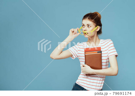 Female student with books in hands on a blue background and yellow glasses model hairstyle cropped view Female student with books in hands on a blue background and yellow glasses model hairstyle cropped view 79691174