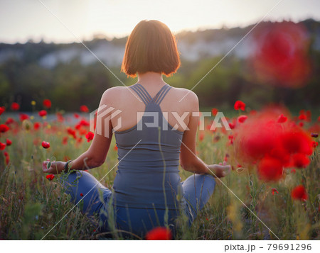 A beautiful woman meditates on a poppy field at sunset 79691296