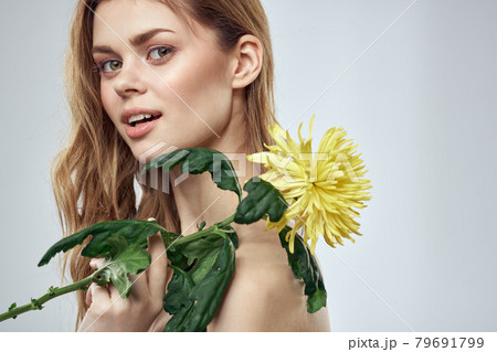 Portrait of a beautiful woman with a yellow flower on a light background charming smile model red hair Portrait of a beautiful woman with a yellow flower on a light background charming smile model red hair 79691799