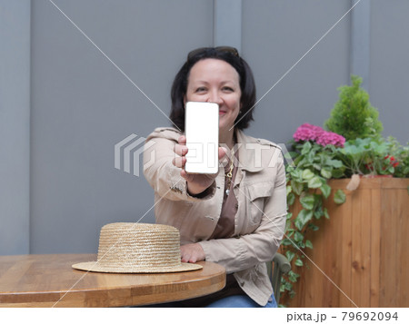 Happy woman sits at a table in a cafe and shows the white screen of the phone. 79692094