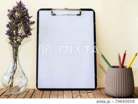 Plain Office Clipboard With Stack Of Pens In A Holder Beside A Flower Vase. Empty Paper Sheet With Colorful Pencils Next To Floret Container Placed On Table. Plain Office Clipboard With Stack Of Pens In A Holder Beside A Flower Vase. Empty Paper Sheet With Colorful Pencils Next To Floret Container Placed On Table. 79693059
