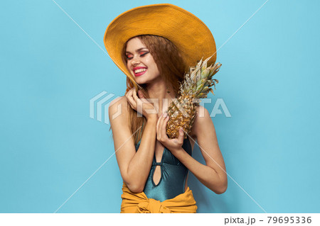 Cheerful woman beach hat exotic fruits swimsuit lifestyle blue background Cheerful woman beach hat exotic fruits swimsuit lifestyle blue background 79695336