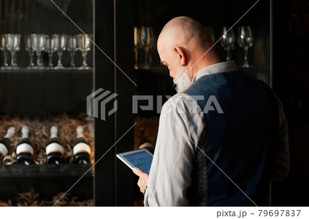 liquor store owner with a digital tablet standing near a rack of wine samples . liquor store owner with a digital tablet standing near a rack of wine samples . 79697837