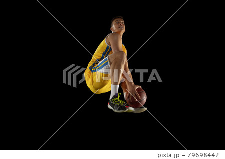 Jump shot. Basketball player with a ball in action and motion isolated on dark black studio background. Advertising concept. Strong Caucasian athlete practicing with basketball ball. Jump shot. Basketball player with a ball in action and motion isolated on dark black studio background. Advertising concept. Strong Caucasian athlete practicing with basketball ball. 79698442