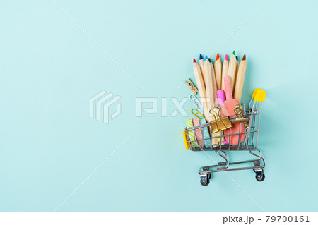 Buying school supplies, pencils, tape, notebook and crayons. Stationery for kids in a shopping cart on blue turquoise background, copy space. Back to school concept. Flat lay top view. Buying school supplies, pencils, tape, notebook and crayons. Stationery for kids in a shopping cart on blue turquoise background, copy space. Back to school concept. Flat lay top view. 79700161