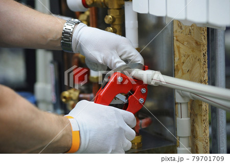 Plumber hands in gloves cut plastic pipe with the pipe cutter 79701709