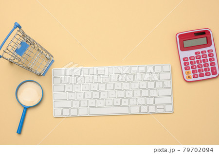 white wireless keyboard and empty shopping cart, magnifier on beige background, budget analysis concept 79702094